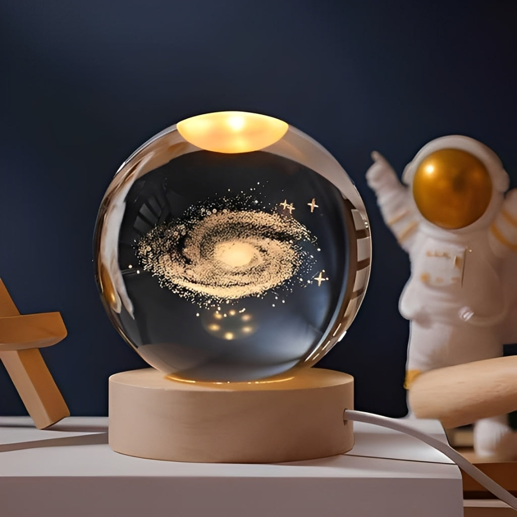 Decorative glass sphere with galaxy design on a wooden base, next to an astronaut figurine.